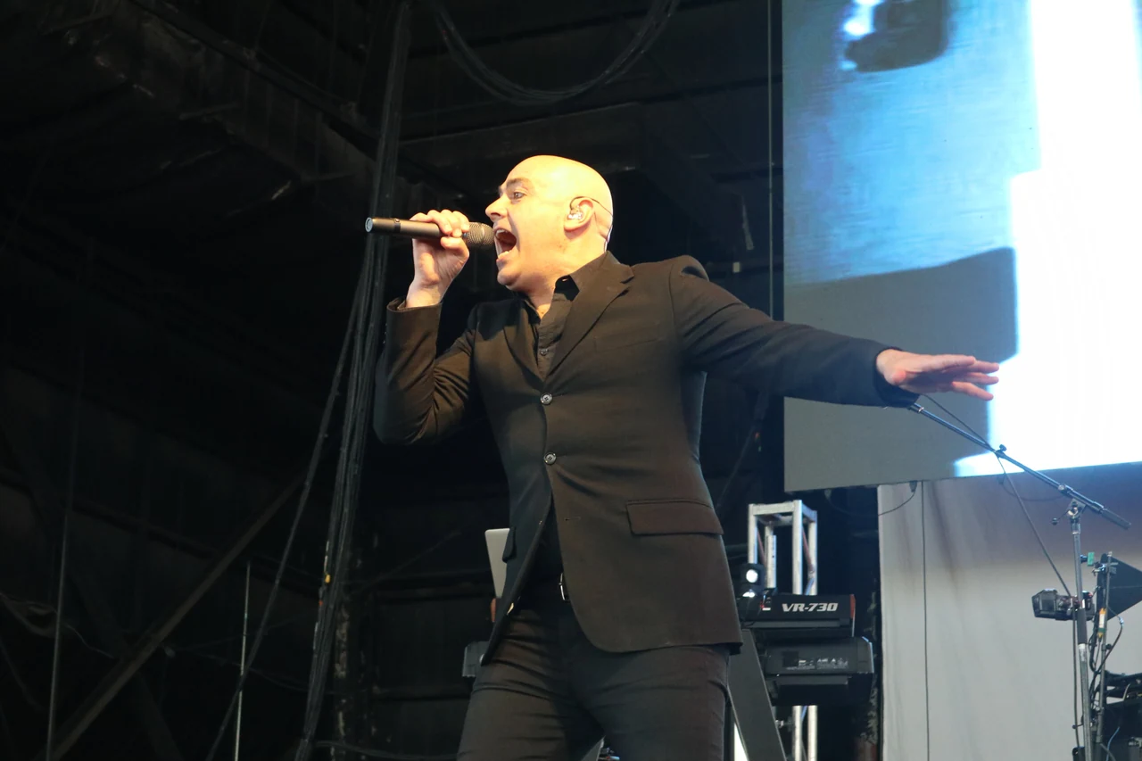 Peter Furler sings with one arm extended under concert lighting.