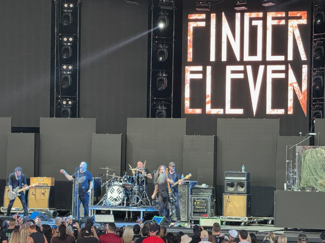 Finger Eleven performing in daylight beneath their name, with the audience along the front of the stage.
