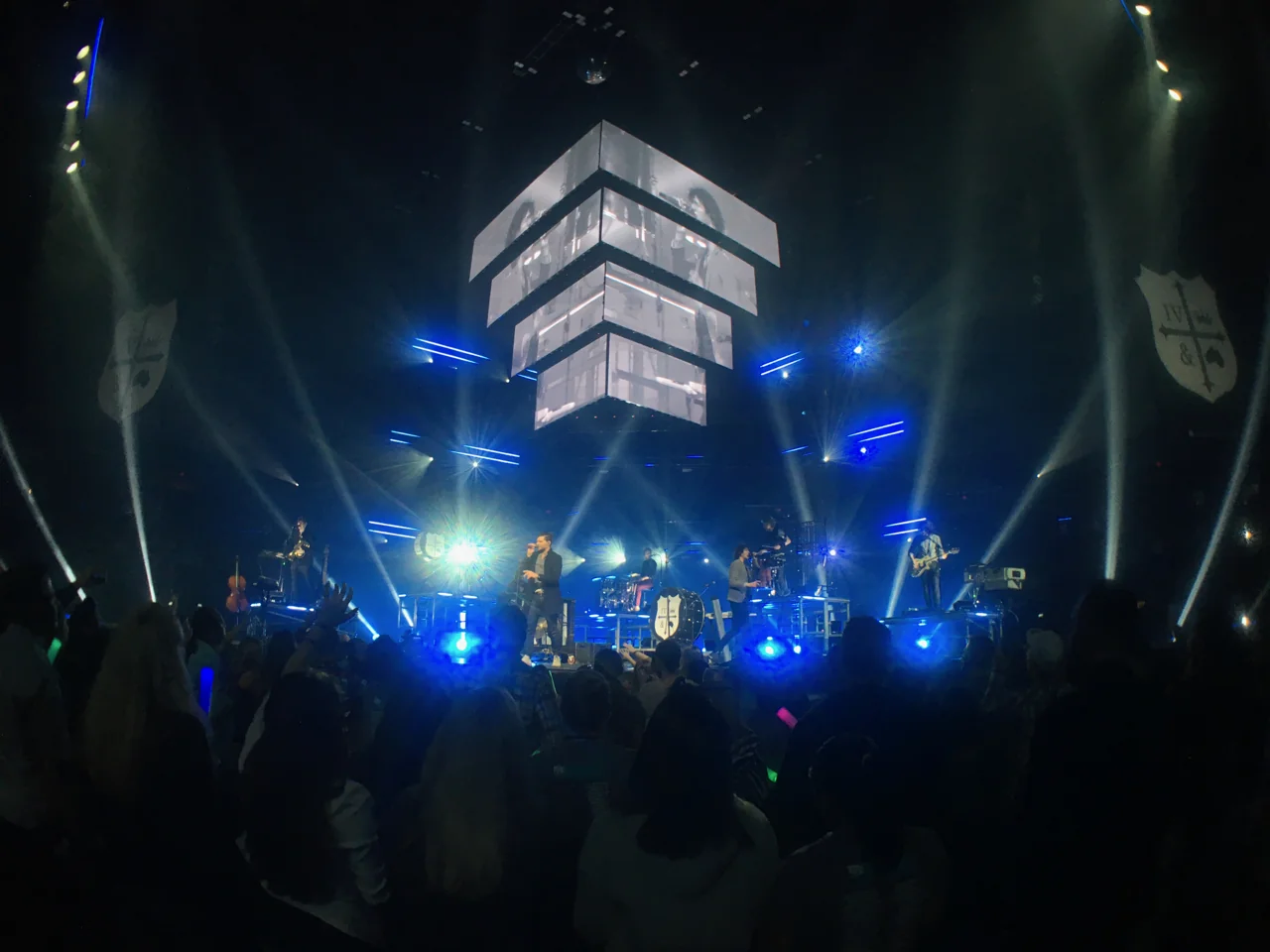For KING & COUNTRY performing beneath a suspended stack of rectangular video screens, with blue and white stage beams, band crests on side banners, and audience silhouettes below.
