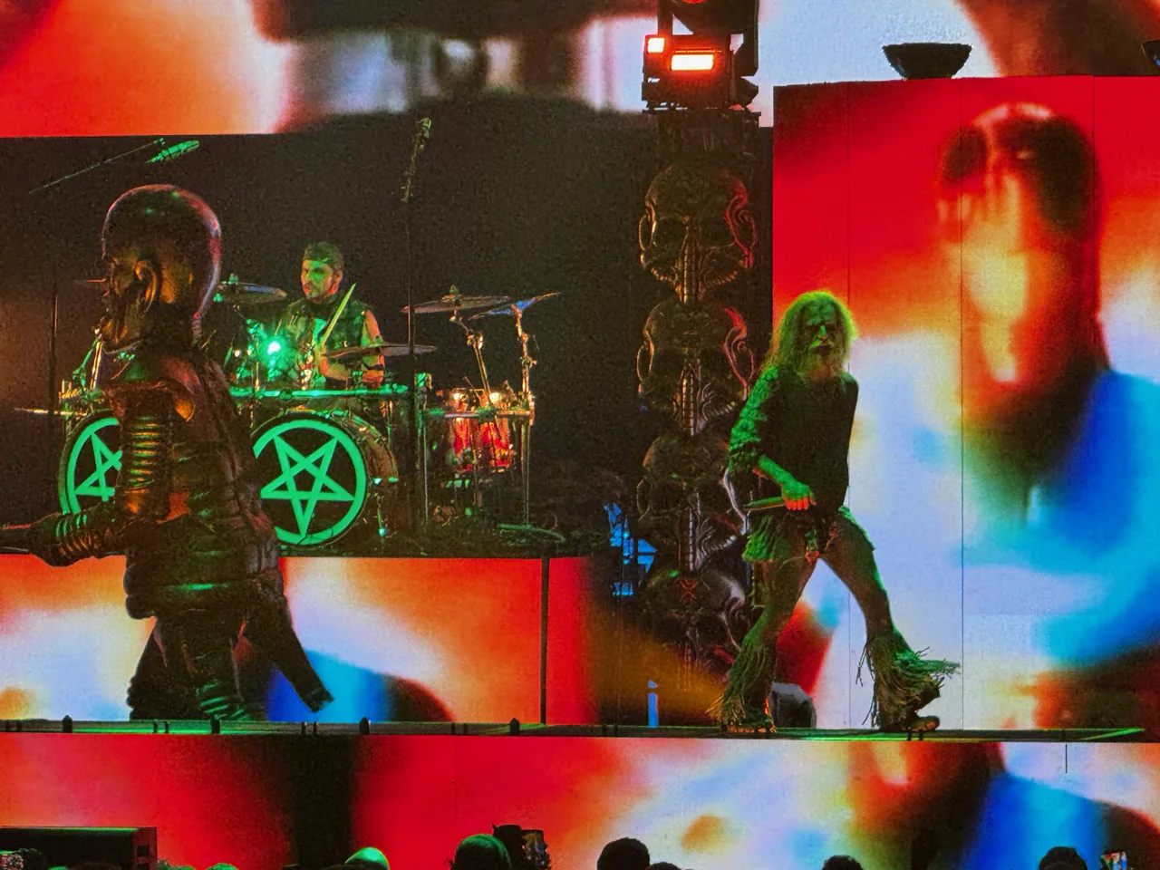 Rob Zombie singing beside the drum riser against a multicolored backdrop.