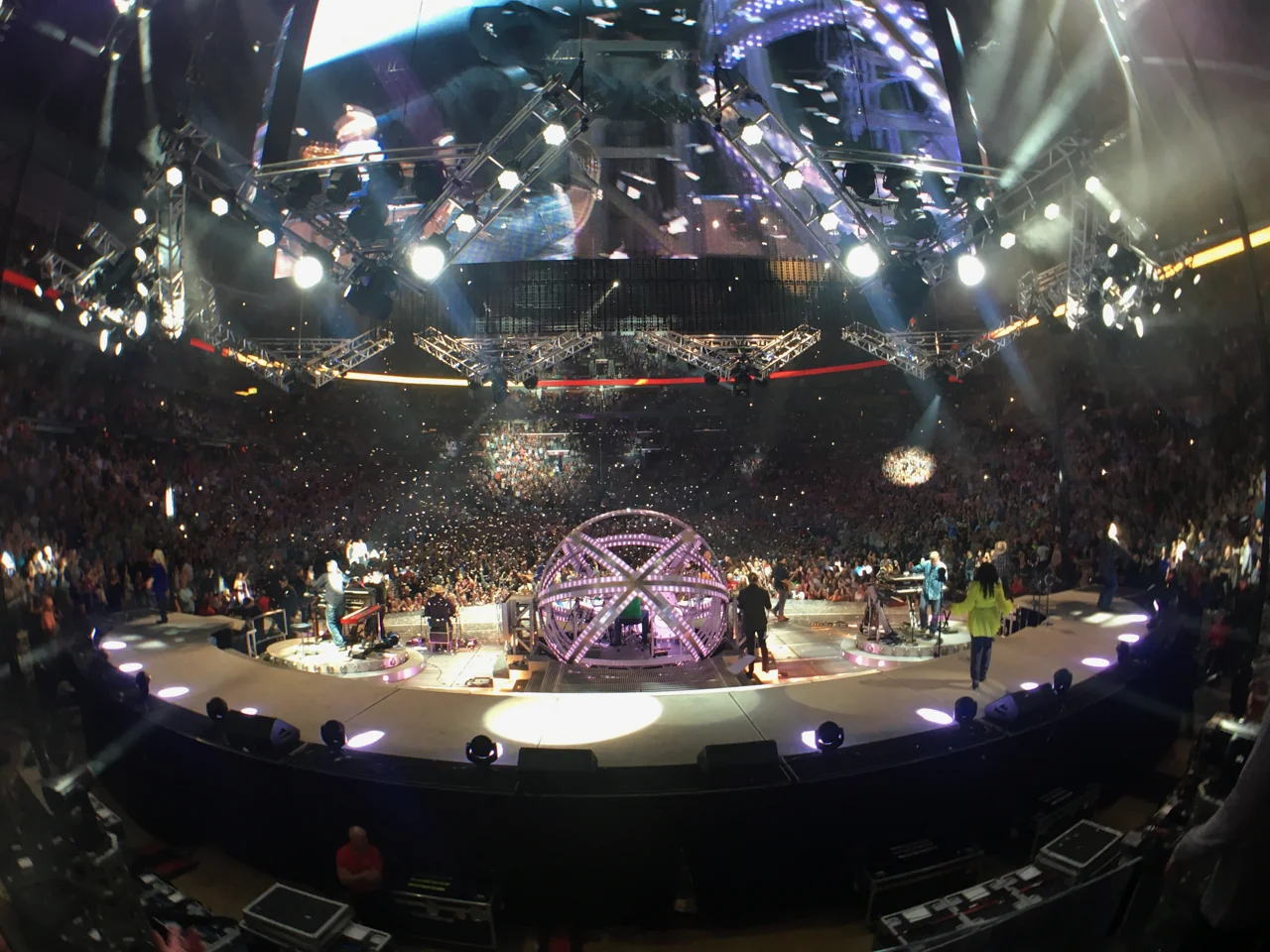 A wide view of Garth Brooks and his band on an arena stage surrounded by the audience, with confetti falling around a purple spherical drum enclosure.