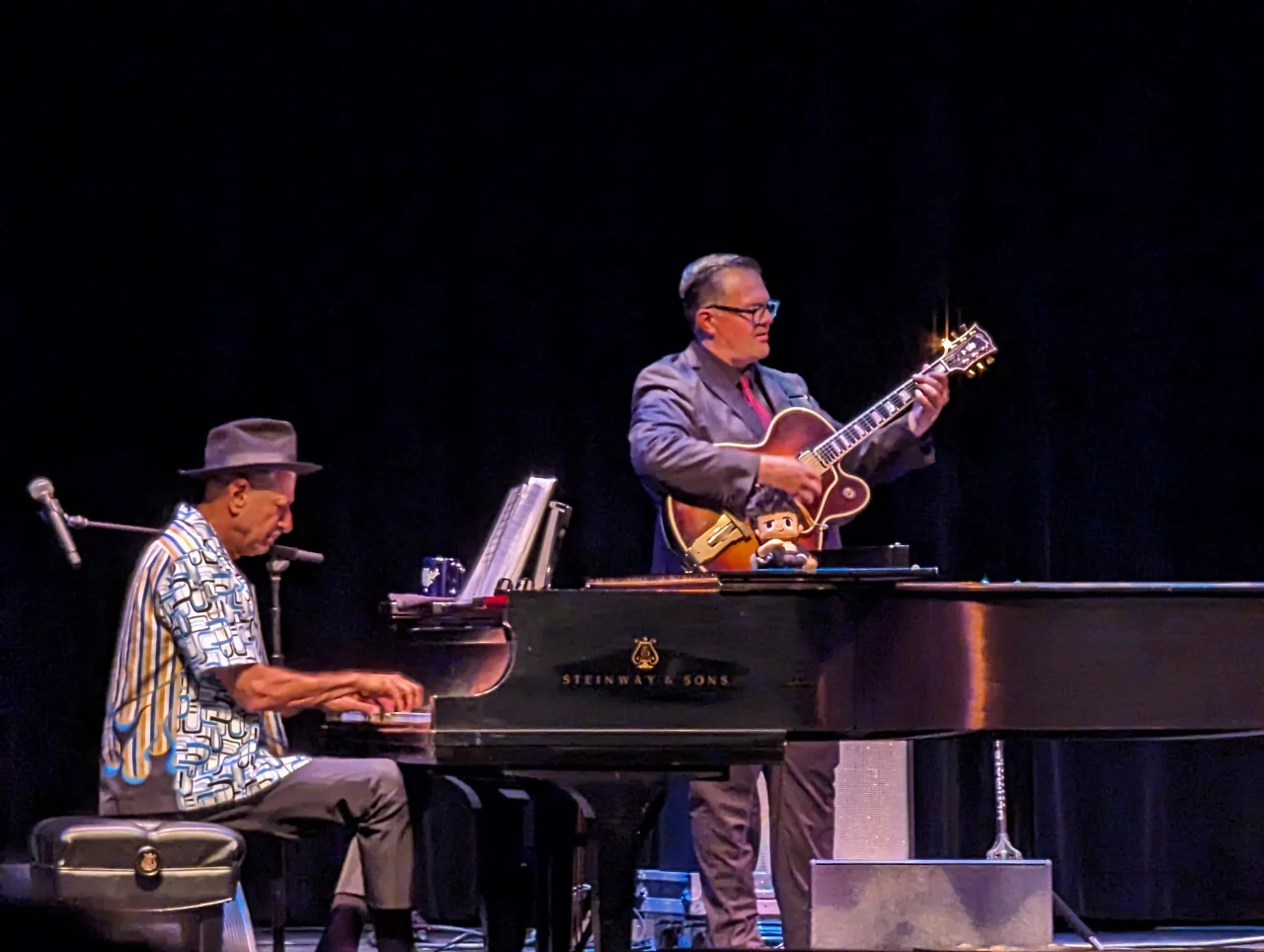Jeff Goldblum playing a Steinway grand piano beside a guitarist.