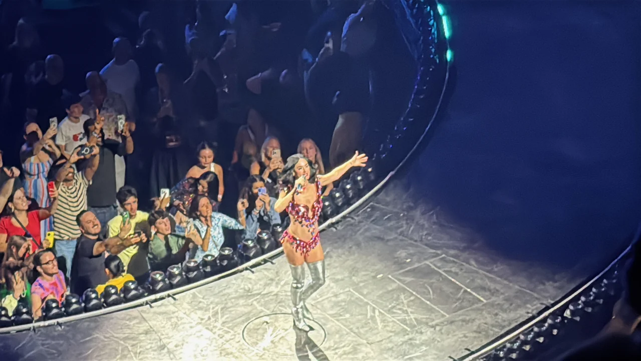 Katy Perry singing on the curved runway beside the audience.