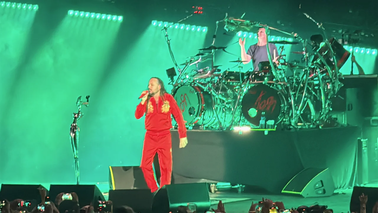 Jonathan Davis singing in a red tracksuit against green light, with Korn’s drummer behind him.
