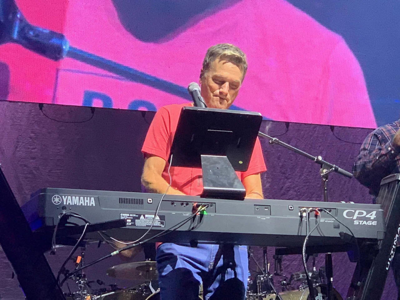 Michael W. Smith playing a Yamaha keyboard in a red shirt, with his enlarged image behind him.