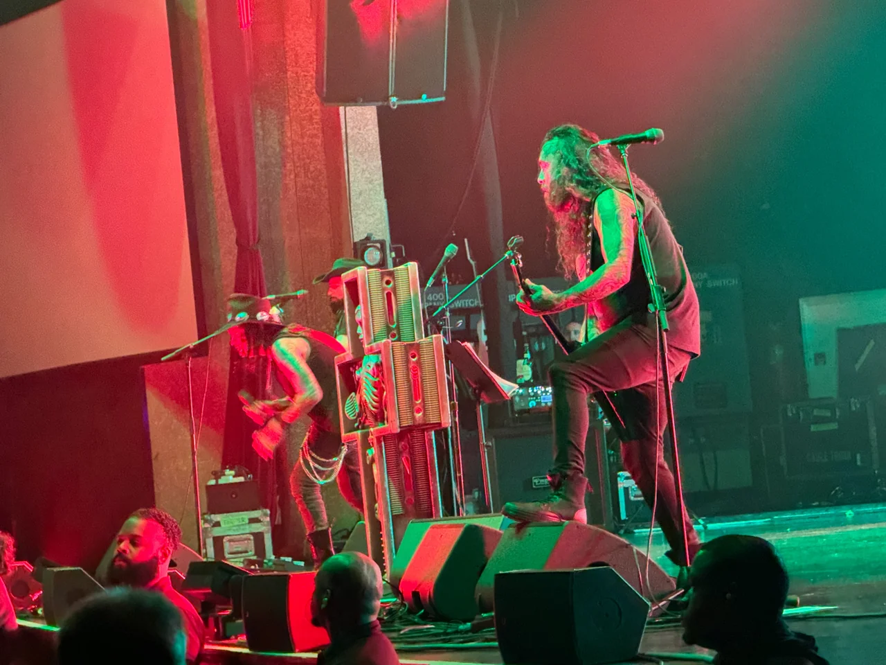Ministry performing under red and green light beside a sculptural microphone stand.