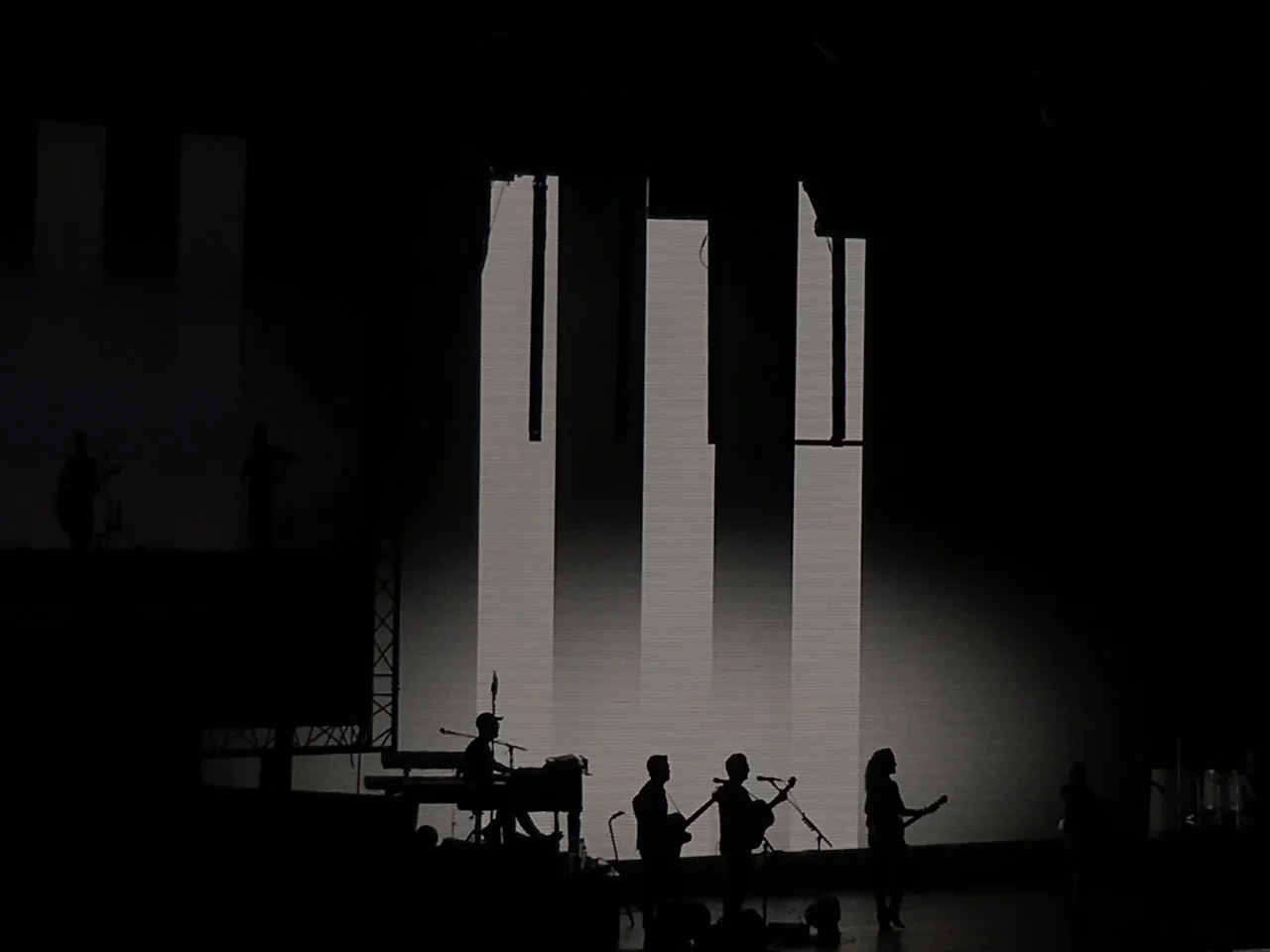 The Chicks and their backing musicians in silhouette beneath tall white shapes on the stage screens.