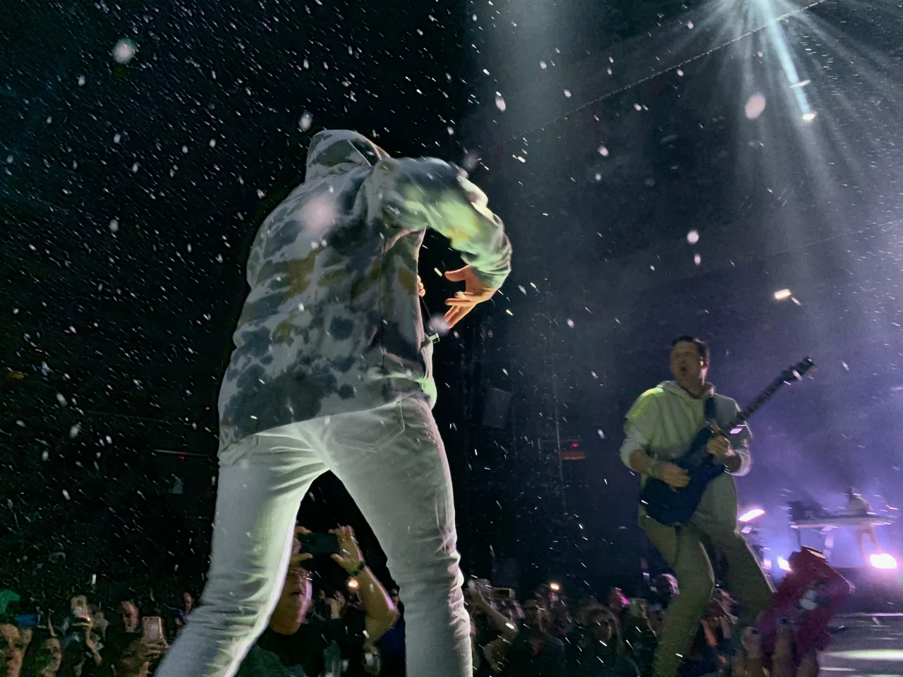 TobyMac and his guitarist performing close to the audience beneath falling white confetti and a bright overhead spotlight.
