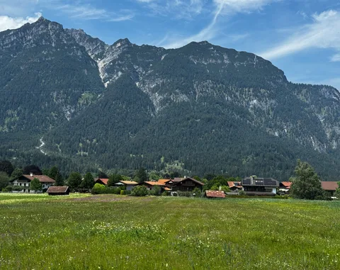 Houses and a meadow beneath a steep mountain wall.