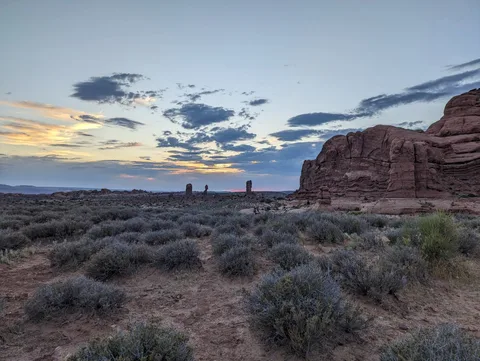 A path through scrub toward three upright rocks at dusk.